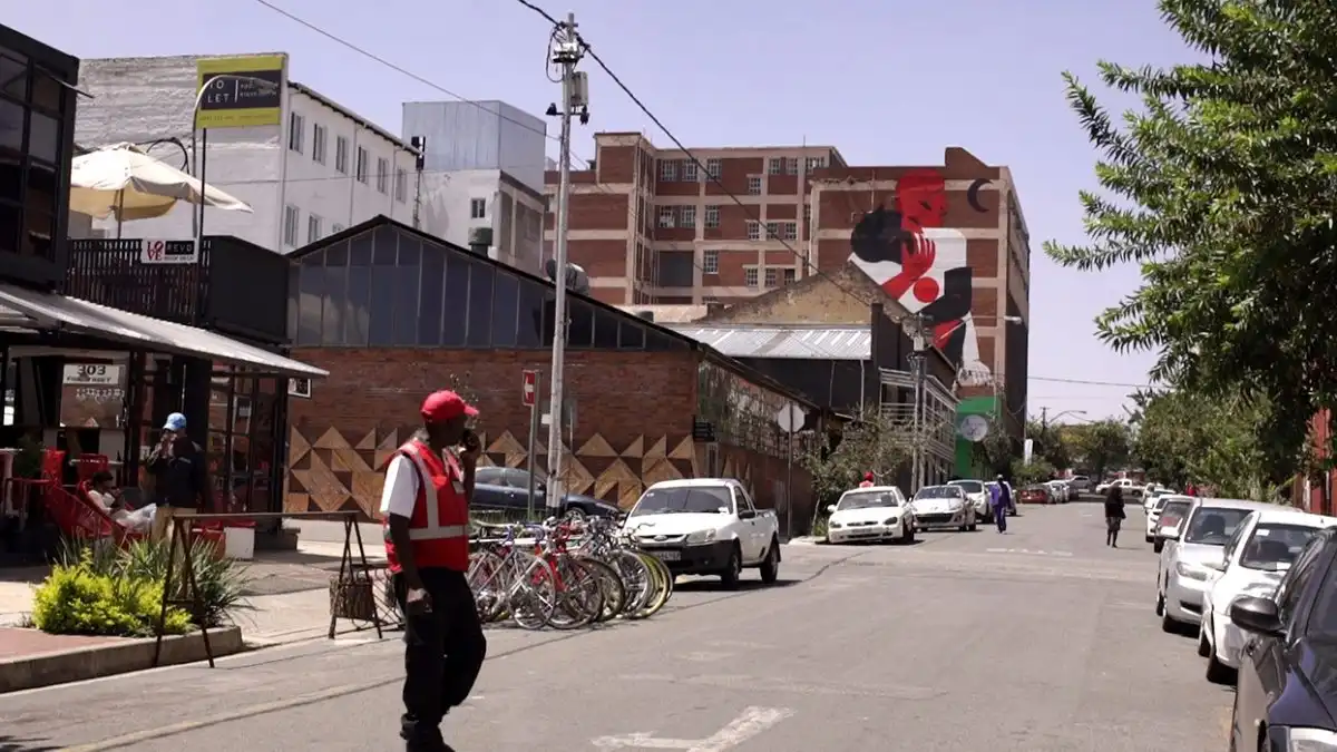 Street scene with a crossing guard, parked cars, bicycles, and a large mural on a brick building in the background.