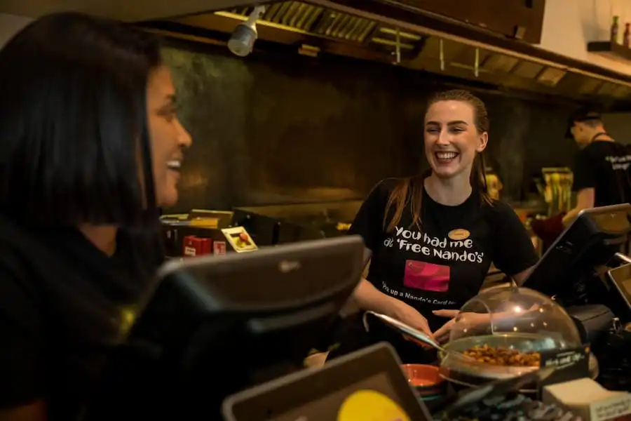 Two Nando's staff members smiling and chatting behind the counter, creating a welcoming and lively atmosphere.